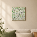 Green Pastures original abstract painting by Alli Cullimore displayed in a lounge — 41×41cm acrylic on canvas with splattered dark and light greens, black and earth tones on a white textured base